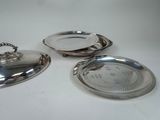 three silverplated dishes on a white table with a silver lid