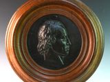 une photo d'un portrait en bronze représentant un homme, dans un cadre en bois