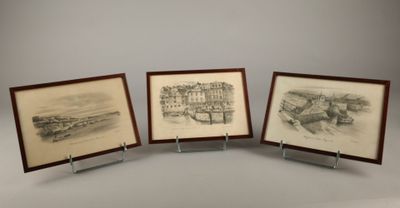 trois dessins encadrés représentant une ville et un bateau, posés sur une table