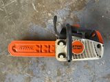 une tronçonneuse orange et noire posée sur un sol en béton