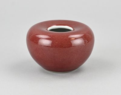 une image représentant un vase rouge posé sur une surface blanche
