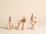 trois petites figurines représentant des personnes assises sur une surface blanche