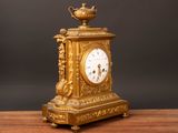 a gold clock sitting on a wooden table with a black background