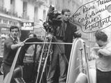 photographie en noir et blanc d'un homme debout à côté d'une voiture sur laquelle est posée une caméra
