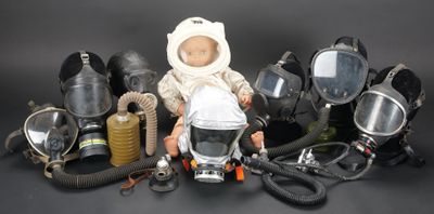 une poupée portant un masque à gaz, entourée de masques à gaz