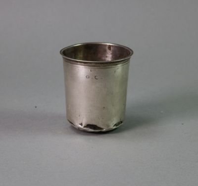 a small silver cup with a handle on a gray surface
