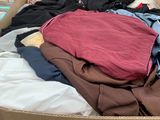 une boîte en carton remplie de nombreux vêtements, posée par terre