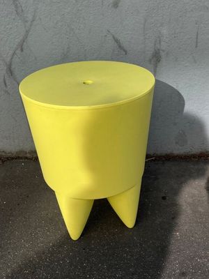 a yellow stool sitting on the sidewalk next to a white wall