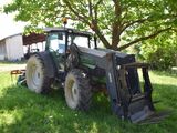 a tractor that is parked in the grass near a tree