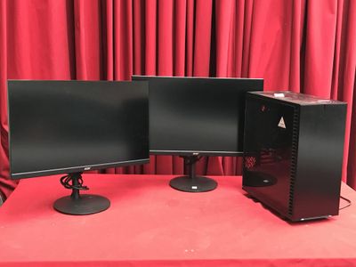 deux écrans d'ordinateur posés sur une table, devant des rideaux rouges