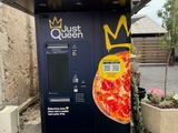 un distributeur automatique sur lequel est posée une pizza, devant un immeuble
