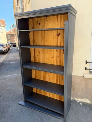 tall grey bookcase with wooden shelves in front of a building