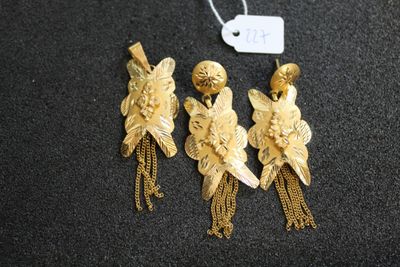 trois boucles d'oreilles dorées ornées de pompons et d'une étiquette, sur un fond noir