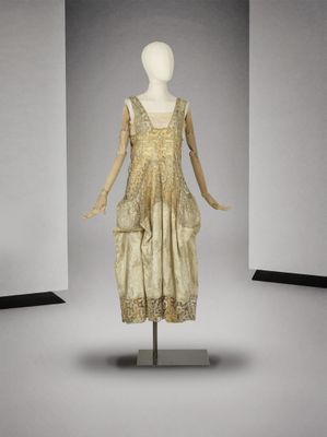 une photo d'un mannequin portant une robe dorée, posé sur un socle