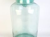 un bocal en verre vert muni d'un couvercle, posé sur une surface blanche