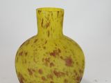 a yellow vase with brown spots sitting on a white surface