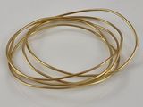 quatre bracelets en fil métallique doré superposés les uns sur les autres sur une surface blanche
