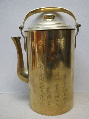 a brass tea pot with a handle on a white surface