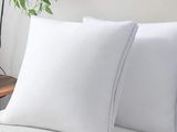 two white pillows sitting on top of a bed next to a plant