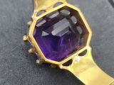 a close up of a gold bracelet with a purple stone on it
