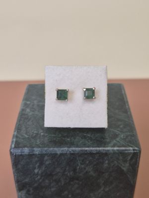 a pair of emerald earrings sitting on top of a marble block