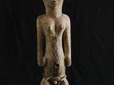 une statue en bois représentant un homme debout sur un fond noir