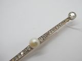 une photo d'une broche en forme de barre, ornée d'une perle blanche et de diamants