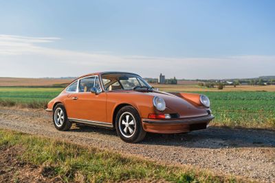 an orange porsche parked on the side of a dirt road next to a field