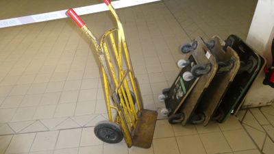 a hand truck that is sitting on the floor next to a pile of luggage
