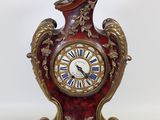 une horloge rouge et dorée posée sur une surface blanche