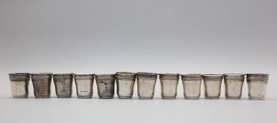 six verres à shot en argent alignés en rangée sur une surface blanche