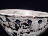 un bol blanc percé de trous sur une surface noire