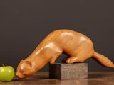 a wooden sculpture of a cat sniffing a green apple