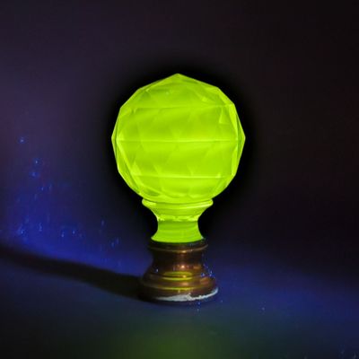 un vase en verre vert brillant posé sur un socle en bois, sur fond sombre