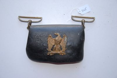 un vieux sac à main orné d'un aigle doré, accroché au mur
