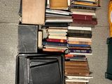 a pile of books on the floor next to a suitcase and a clock