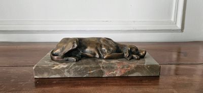 une statue en bronze représentant un chien couché sur un socle en marbre