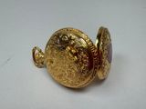 a gold pocket watch with a red stone in it
