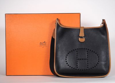 un sac à main noir et beige, avec une boîte orange en arrière-plan