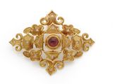 a close up of a gold broochle with a red stone