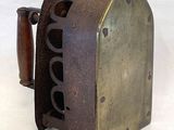 un objet métallique à l'ancienne, muni d'un manche en bois, posé sur une surface blanche