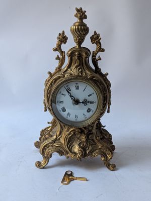 a gold clock sitting on a white surface with a key