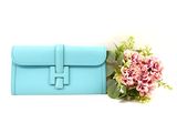 a blue clutch bag next to a bouquet of flowers on a white surface