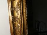 un miroir au cadre doré ouvragé, dans une pièce sombre où se trouve une chaise