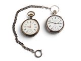 deux vieilles montres de poche attachées à une chaîne, posées sur une surface blanche
