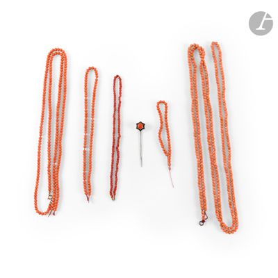 plusieurs colliers de perles orange et une paire de ciseaux posés sur une surface blanche