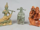 three small statues of people sitting on top of a white surface