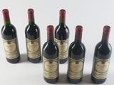 six bottles of wine are lined up in a row on a white surface