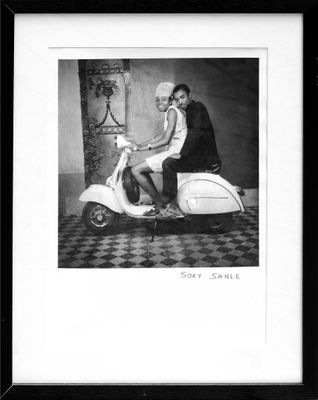 black and white photograph of a woman sitting on a motor scooter
