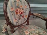 a chair with a floral upholstered back and a wooden arm rest